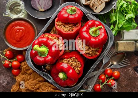 Poivrons paprika farcis à la cloche rouge dans un pot de cuisson en fer avec divers ingrédients sur le côté Banque D'Images