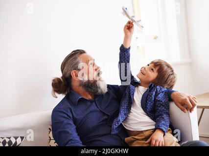 Des manœuvres aériennes incroyables avec grand-père. Coupe courte d'un jeune garçon assis sur ses grands-pères en toile jouant avec un jet jouet. Banque D'Images