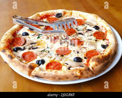 Une pizza fraîchement cuite avec des champignons, des saucisses et des olives se dresse sur une table en bois. Gros plan Banque D'Images