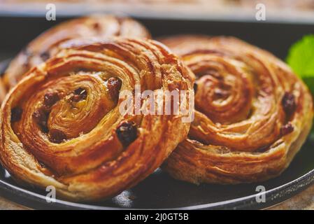 Gros plan sur le gâteau au petit pain à la cannelle avec garniture aux raisins secs servi sur l'assiette noire Banque D'Images