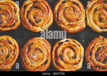 Feuilleté maison aux petits pains à la cannelle et aux raisins secs placés au four fer à repasser Banque D'Images