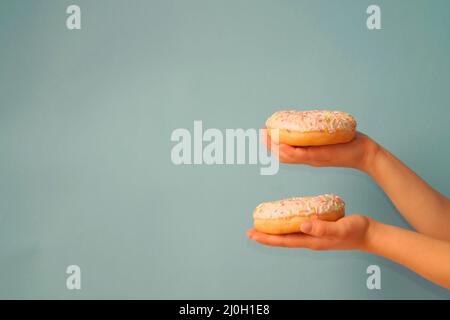 L'enfant tient dans ses mains deux beignets avec des arrosettes multicolores, sur un fond gris-bleu. Concentrez-vous sur le donut supérieur. Les mains sont décalées sur le bord Banque D'Images