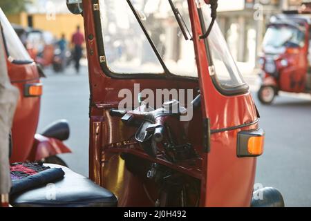 Tuk tuk rouge garé contre la rue animée. Populaire moto à trois roues au Sri Lanka. Banque D'Images