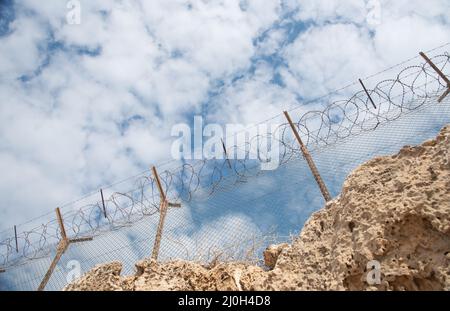 Clôture de sécurité avec fil barbelé contre un ciel bleu nuageux Banque D'Images
