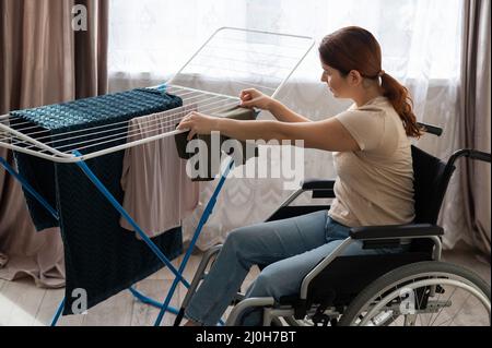 Une femme caucasienne dans un fauteuil roulant pend une lessive humide sur un sèche-linge. Banque D'Images