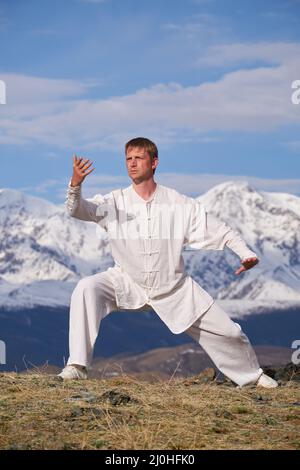 Wushu maître dans un uniforme blanc de sport d'entraînement kungfu dans la nature sur fond de montagnes enneigées. Banque D'Images