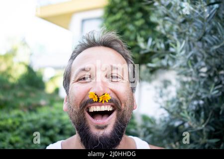 Drôle d'homme avec fleur dans le nez riant Banque D'Images