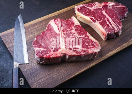 Deux steaks de bœuf Wagyu vieilli et sec, crus, sont offerts en gros plan sur un panneau en bois de conception moderne avec un couteau japonais gyuto