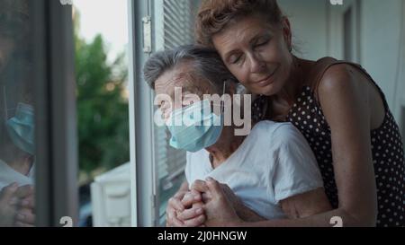 Fille mature rendant visite à une mère âgée dans une maison de soins infirmiers. Une fille âgée encadre sa mère de 90 ans sous un masque médical alors qu'elle est debout Banque D'Images