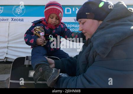 19 mars 2022, Siret, Roumanie: Une mère aide sa fille avec ses chaussures, la petite fille est fatiguée après avoir fait un voyage pour traverser la frontière. Environ 3 mille personnes arrivent quotidiennement à Siret, en Roumanie, pour se réfugier contre la violence causée par la guerre entre la Russie et l'Ukraine. Dans cette ville frontalière, un couloir d'aide humanitaire a été organisé entre diverses organisations civiles et étatiques. Les personnes qui fuient l'Ukraine sont principalement des femmes, des enfants et des adultes plus âgés. Lorsqu'ils franchissent la frontière, les gens reçoivent de l'aide médicale, psychologique, alimentaire, de transport et d'hébergement. Grâce à l'aide des bénévoles, Banque D'Images