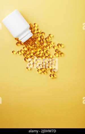 Les capsules d'huile de poisson Golden Omega-3 ont été déversées d'un pot sur fond jaune. Espace libre Banque D'Images