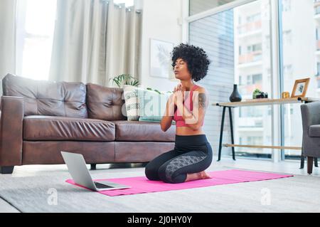 Ces cours virtuels m'ont vraiment beaucoup enseigné. Photo d'une belle jeune femme utilisant son ordinateur portable tout en pratiquant le yoga à la maison. Banque D'Images