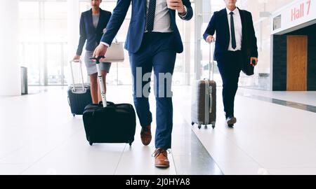 Notre entreprise nous oblige à voyager. Plan court de trois hommes d'affaires méconnus qui marchent et tirent des valises au bureau pendant le Banque D'Images