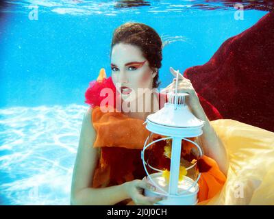 Portrait de mode sous-marin de belle blonde jeune femme en robe rouge avec lampe Banque D'Images