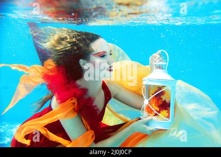 Portrait de mode sous-marin de belle blonde jeune femme en robe rouge avec lampe Banque D'Images