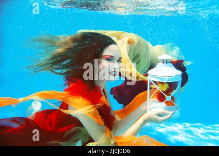 Portrait de mode sous-marin de belle blonde jeune femme en robe rouge avec lampe Banque D'Images