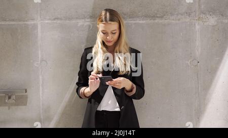 Femme d'affaires parcourant un téléphone portable près d'un mur en béton Banque D'Images