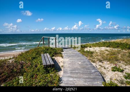 Une promenade en bois menant à la plage mène à travers les dunes de sable et les arbustes à une plage idyllique Banque D'Images