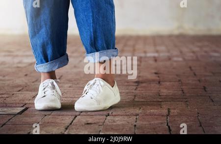 Chaussures, danse. Photo courte d'une personne méconnaissable debout sur un sol en briques avec des baskets blanches et des jeans bleus. Banque D'Images