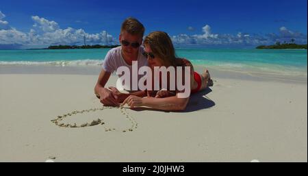 Couple heureux se posant sur la côte et tirant un coeur sur le sable dans les beaux Maldives Banque D'Images