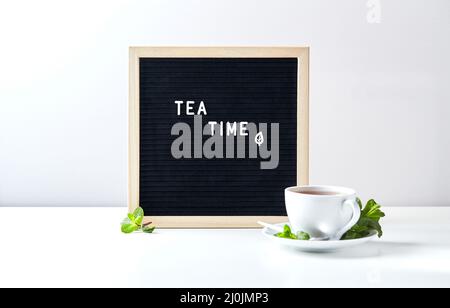 Temps de thé. Tableau de lettres noir avec texte sur la table avec une tasse de thé en verre avec des feuilles de menthe Banque D'Images