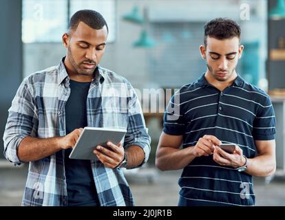 Pris dans un monde connecté. Photo de deux jeunes concepteurs utilisant des appareils numériques dans un bureau. Banque D'Images