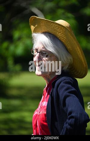 La femme âgée a un visage froissé et des lignes causées par l'exposition au soleil. Elle porte un chapeau de paille sur ses cheveux blancs et se perd dans la pensée à l'extérieur Banque D'Images