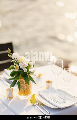 Réception de table de dîner de mariage. Bain transparent en verre avec des citrons en tranches et un bouquet d'Alstromeri blanc, sur la table contre Banque D'Images