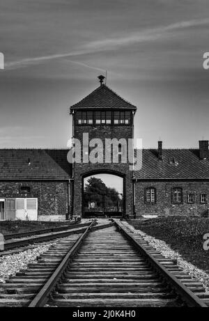 Vue en noir et blanc du portier et des pistes de train au camp de concentration d'Auschwitz en Pologne Banque D'Images