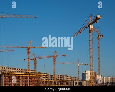 Certaines grues à tour sur fond de ciel bleu et ouvriers et constructeurs industriels avec casque en béton uniforme pour le chantier Banque D'Images