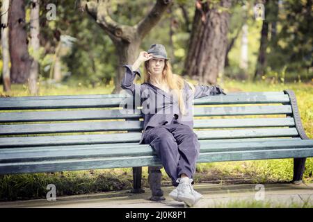 Une femme vêtue de lilas et un chapeau est assise sur un banc de parc par temps ensoleillé Banque D'Images