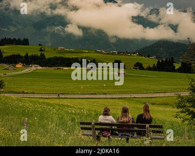 Des amies de sexe féminin assises sur un banc sur un pré vert à Bolsterlang Banque D'Images