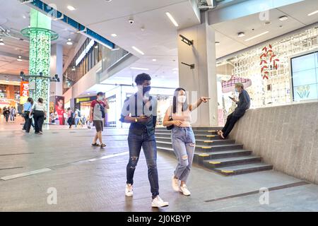 Femme asiatique portant un masque pointant vers l'avant tout en marchant avec un ami dans un centre commercial Banque D'Images