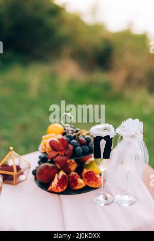 Une table peinte avec une bibliothèque avec des fruits et des verres pour champagne dans les costumes de la mariée et du marié. Banque D'Images