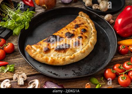 Pizza calzone sur une assiette noire avec des légumes Banque D'Images