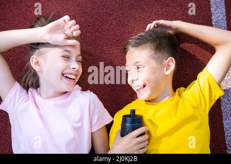 Thème de style de vie de sport pour enfants. Joyeux garçon et fille adolescents reposent joyeusement sur la couverture en caoutchouc de la piste de course du stade et effacer Banque D'Images