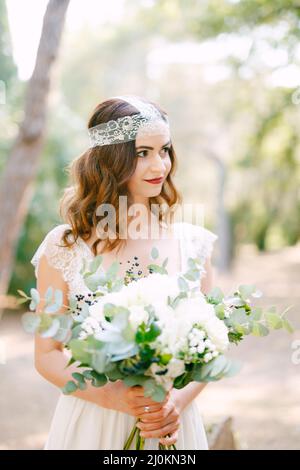 La mariée tient dans ses mains un bouquet de roses, des branches d'eucalyptus, des fleurs blanches délicates et des baies sombres Banque D'Images