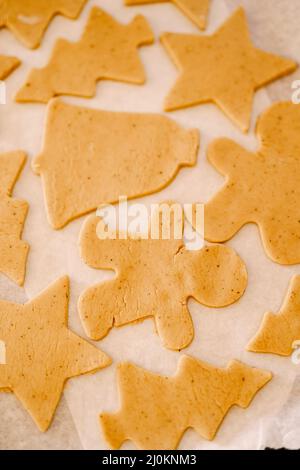 Processus de fabrication de biscuits faits maison ou de pain d'épice sous différentes formes. Les biscuits à la pâte crue reposent sur une plaque de cuisson recouverte de paillis Banque D'Images