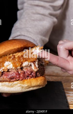 En tenant deux mains un hamburger de bœuf incroyable avec beaucoup de fromage à la crème et des oignons caramélisés en trempant l'index dans le fromage à la crème Banque D'Images