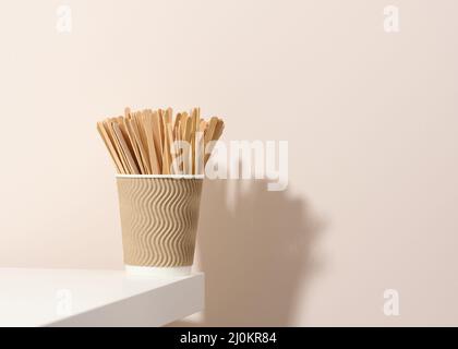 Tasses en carton et bâtonnets en bois sur une table blanche, fond beige. Vaisselle écologique, sans gaspillage Banque D'Images