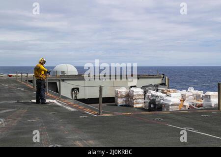 MER DES PHILIPPINES (18 mars 2022) Aviation Boatswain's Mate (Handling) 1st classe Christopher Farrell, de Salisbury, N.C., signale à un exploitant d'ascenseur d'abaisser le fret du pont de vol du porte-avions de la classe Nimitz USS Abraham Lincoln (CVN 72) À la baie hangar lors d'un réapprovisionnement vertical en mer avec le navire de cargaison sèche et de munitions USNS Alan Shepard (T-AKE 3) du Commandement du Seallift militaire. Abraham Lincoln Strike Group est sur un déploiement prévu dans la zone d'exploitation de la flotte américaine 7th afin d'améliorer l'interopérabilité par le biais d'alliances et de partenariats tout en servant de réponse prête à l'emploi Banque D'Images