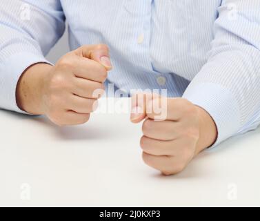 Deux mains de femme repliées dans un poing sur une table blanche.Leader strict, agression et pression sur la personne Banque D'Images