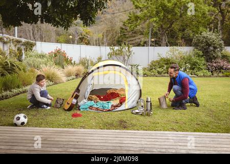 Un père et un fils caucasiens souriant tout en dressant une tente ensemble dans le jardin Banque D'Images