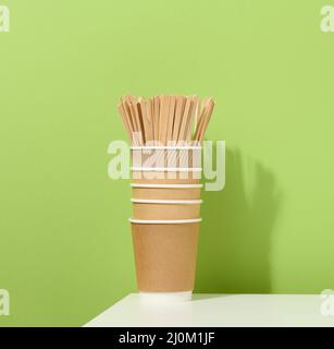 Tasses en carton et bâtonnets en bois sur une table blanche, fond vert. Banque D'Images