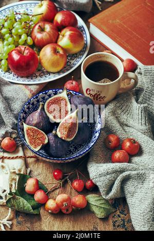 Plat avec figues, pommes et raisins et une tasse de café sur un fond en bois avec des vêtements chauds et douillets, des feuilles d'automne et des pommes. Banque D'Images