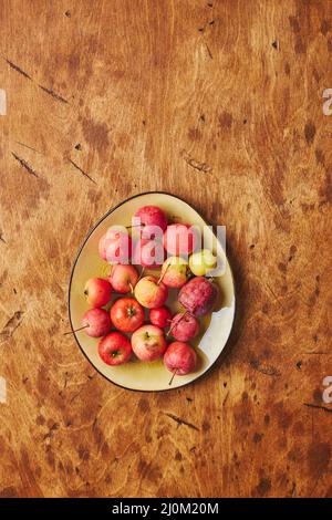 Assiette avec petites pommes rouges - CrabApple, sur fond de bois chaud Banque D'Images