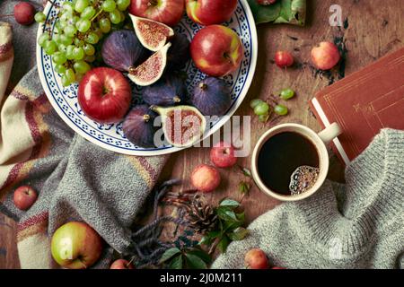 Plat avec figues, pommes et raisins et tasse de café sur fond de bois avec chandail chaud, foulard, feuilles d'automne et pommes. AUT Banque D'Images