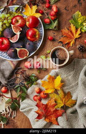 Plat avec figues, pommes et raisins et tasse de café sur fond de bois avec un pull chaud, écharpe, feuilles d'automne et pommes. A Banque D'Images