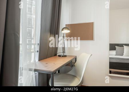 Tables de travail avec chaise blanche, lampe noire et miroir sur le mur dans une chambre Banque D'Images