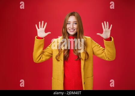 Mignonne et tendre belle-look sympathique redhead femme avec les yeux bleus et les taches de rousseur dans élégant manteau jaune montrant le numéro dix ou ORD Banque D'Images